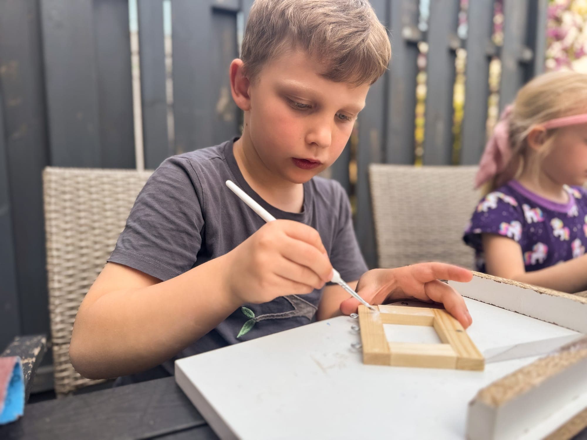 Ein Junge bemalt seinen Holzrahmen mit dem Pinsel