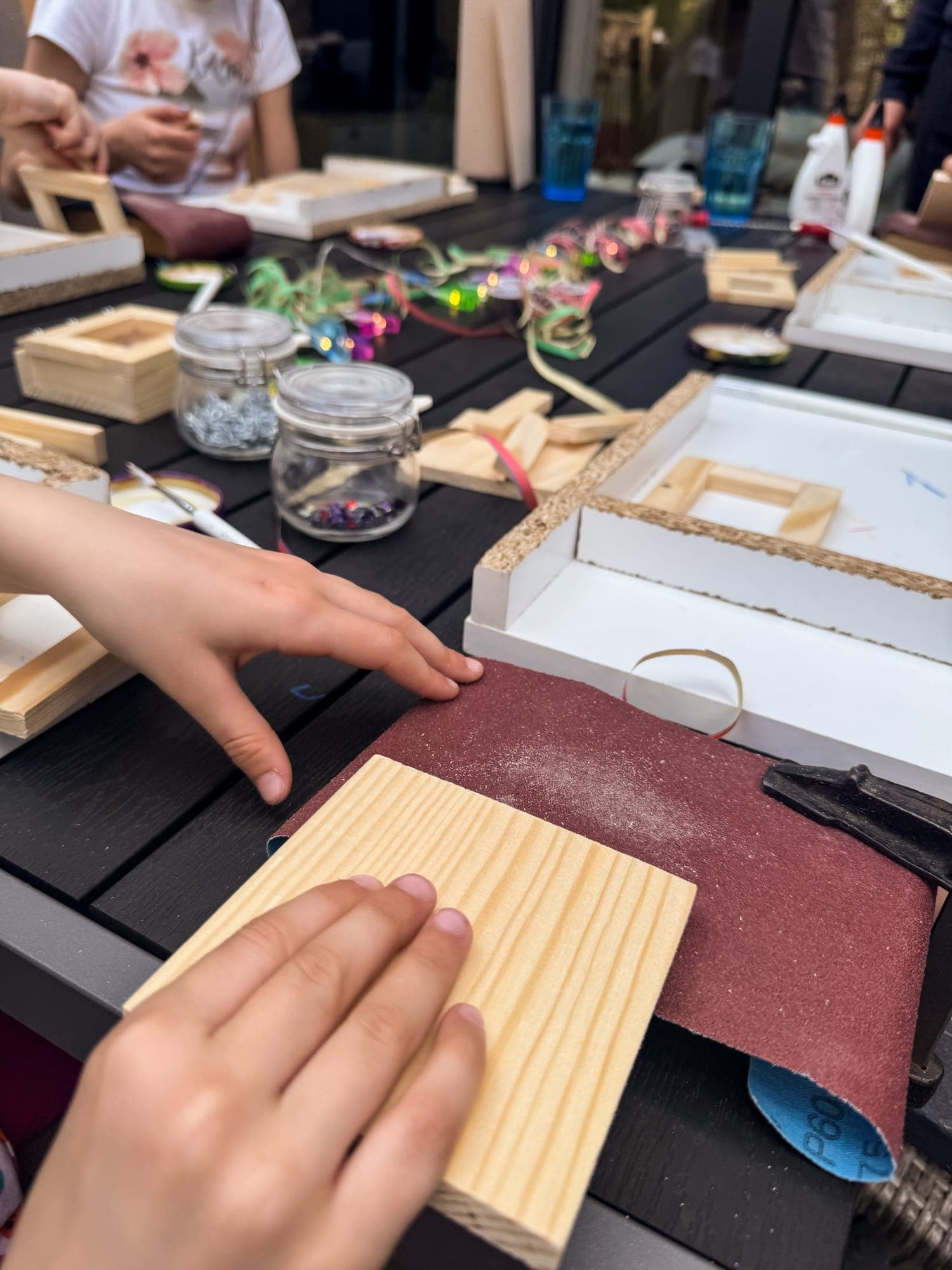 Eine Kinderhand schleift ein Holzbrett auf dem Schleifpapier der Werkbank