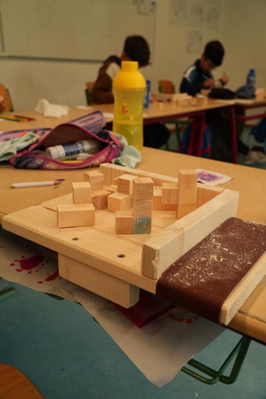 Ein Holzrahmen, in dem Kinder Würfel aus Holzklötzen zusammensetzen